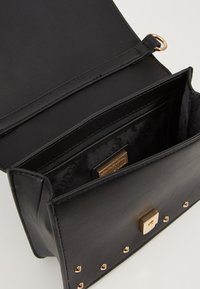 Borsa a tracolla nera in pelle con una superficie liscia, dotata di una chiusura quadrata dorata e borchie metalliche sul fronte. Interno con slot per carte e logo.