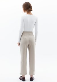 Witte lange mouwen top gecombineerd met hoog getailleerde beige broek en bruine loafers; soepele stof en een getailleerde pasvorm.