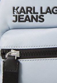 Svetlomodrý nylonový batoh s čiernym logom. Obsahuje zips, kožený akcent a textúrovaný povrch pre vyššiu trvácnosť.