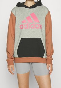 Šedá a rezavá oversized mikina s černou kapsou, na přední straně velké růžové logo Adidas a černé šňůrky na kapuci.