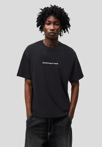 Tricou negru din bumbac cu mâneci scurte și guler rotund, având textul „CHAOTICALLY CUTE” scris cu font alb pe piept.