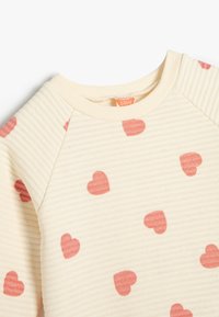 Lichtcrème geribde sweatshirt met roze hartpatronen, voorzien van raglanmouwen en een ronde halslijn. Zachte textuur, casual ontwerp.
