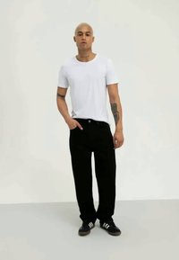 Biała koszulka z krótkim rękawem, czarne luźne spodnie i czarne sneakersy z białymi paskami. Gładki materiał i prosty design.