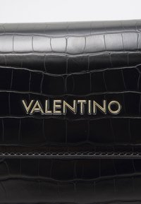 Clutch in pelle nera con texture a coccodrillo, dotata di un prominente logo oro "Valentino". Finitura liscia e forma rettangolare.