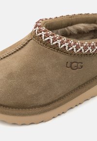 Brun mockasins i mocka med en mjuk inuti, flätad övergångssöm i kräm och rost, samt en texturerad gummisula med vågmönster.