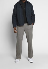 Námořnická modrá lehká bunda s dvěma předními kapsami přes černé polo tričko. Kalhoty s kostkovaným vzorem houndstooth v kombinaci s bílými teniskami.