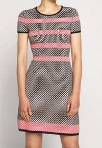 Enganliegendes Kleid mit kurzen Ärmeln, das ein schwarz-beiges dreieckiges Muster zeigt, akzentuiert durch kräftige rosa horizontale Streifen.