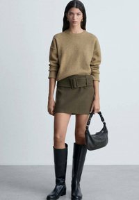Brauner Strickpullover, olivfarbene Rock mit einem Gürtel, schwarze kniehohe Stiefel und eine schwarze Handtasche. Glatte Texturen und minimalistisches Design.
