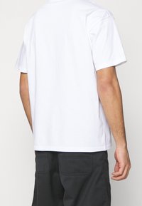 Bílá bavlněná tričko s krátkým rukávem, kulatým výstřihem a uvolněným střihem. Záda jsou jednoduchá, bez viditelného loga nebo vzorů.