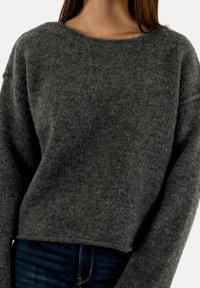 Maglione grigio di lana con collo ampio, spalle scese e orlo corto. Texture morbida e design minimale. Abbinato a jeans scuri.