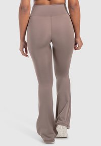 Bruine, high-waisted flared leggings gemaakt van rekbaar materiaal, met een gladde textuur en een subtiele glans, gecombineerd met witte sportschoenen.