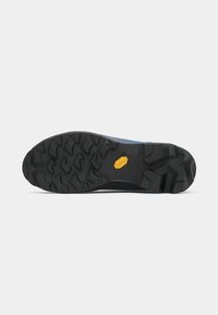 Črna trda podplat čevlja z globokim vzorcem in majhnim rumenim logotipom Vibram na sredini na enobarvni beli podlagi.