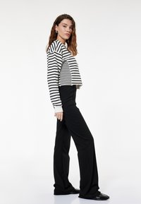 Zwart-wit gestreepte cropped trui met lange mouwen, gecombineerd met hoge taille zwarte rechte broeken en glanzende zwarte schoenen.