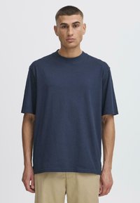 Tricou scurt din stofă moale, de culoare bleumarin, cu mâneci scurte, guler rotund și croială lejeră. Design minimalist, fără modele vizibile.