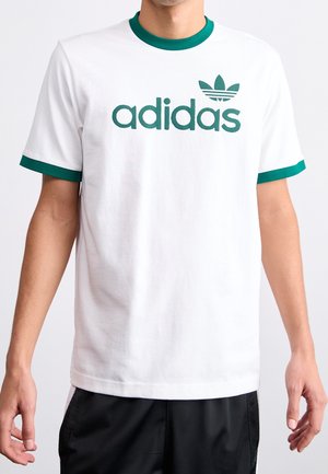 Mann trägt weißes T-Shirt mit grünem Adidas-Logo und grüner Einfassung am Kragen und an den Ärmeln.