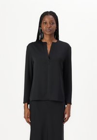 Blusa nera a maniche lunghe con scollo a V e taglio dritto, realizzata in tessuto morbido; indossata con una gonna abbinata, caratterizzata da un design minimalista.