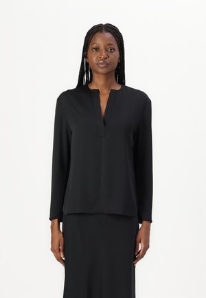 Black long-sleeve blouse with a V-neck and straight cut, made of smooth fabric; worn with a matching skirt, featuring a minimalistic design.