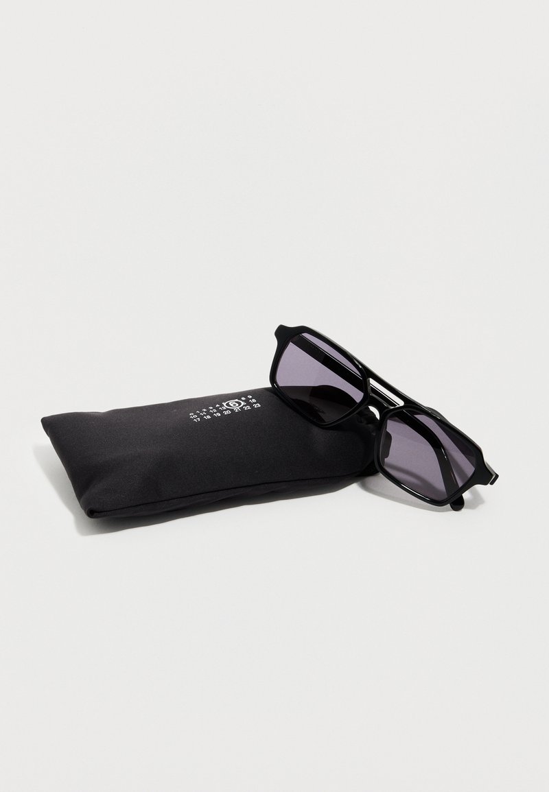 Black square-frame sunglasses with dark lenses resting on a black fabric pouch marked with white numbers and a circular logo.