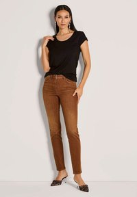 Zwarte top met korte mouwen gecombineerd met bruin aansluitende jeans. De outfit heeft een soepele textuur en een luipaardprint op de hakken voor contrast.