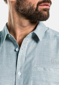 Lichtgroen gestreept overhemd met knopen, voorzien van een klein patch pocket, witte knopen en een kraag. Het materiaal lijkt ademend en textuurrijk.