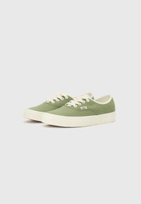 Gröna canvas sneakers med beige snörning, gummisulor och en vit randdetalj längs kanterna. Har en liten logotyp på sidan.