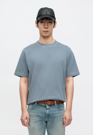 Grå bomuld T-shirt med korte ærmer og rund hals. Kombineret med lyseblå jeans og en sort læderkasket. Enkel og afslappet design.