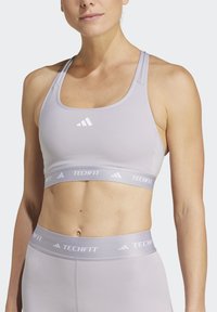 Lichtgrijze sportbeha met een ronde halslijn, brede banden en een gestructureerde tailleband met het label "TECHFIT." Bevat het Adidas-logo in het wit.