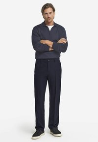 Granatowa koszula polo z długim rękawem i zapinanym kołnierzykiem, połączona z ciemnymi spodniami i czarnymi butami wsuwanymi. Gładka tkanina, klasyczny krój.