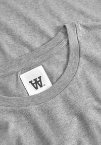 T-shirt in cotone grigio con scollatura rotonda e bordino a costine. Presenta un'etichetta con un logo nero su sfondo bianco. Tessuto morbido e strutturato.