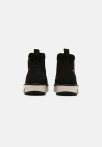 Botas de tobillo de ante negro con suela de goma blanca y negra, que cuentan con una lengüeta en la parte trasera y acentos de logo rojo en los laterales.
