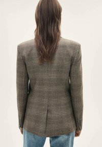 Bruine geruite blazer met gestructureerde schouders en een achterventiel, met een gladde textuur en manchetten met twee knopen, gecombineerd met een blauwe jeans.