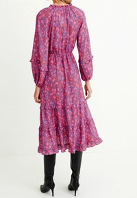 Robe longue à volants avec un imprimé floral rose et violet. Manches froncées avec des poignets élastiques. Tissu léger avec une taille cintrée.