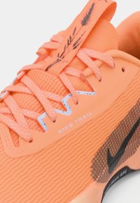 Pomarańczowe sneakersy Nike Trail z teksturowaną siateczkową cholewką, odblaskowymi akcentami i czarnym logo Nike. Posiada plamiste sznurowadła oraz wzór na języku.