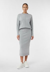 Maglione grigio lavorato a maglia con scollo rotondo e polsini a coste, abbinato a una gonna finta lunghezza al ginocchio. Sneakers bianche completano il look.