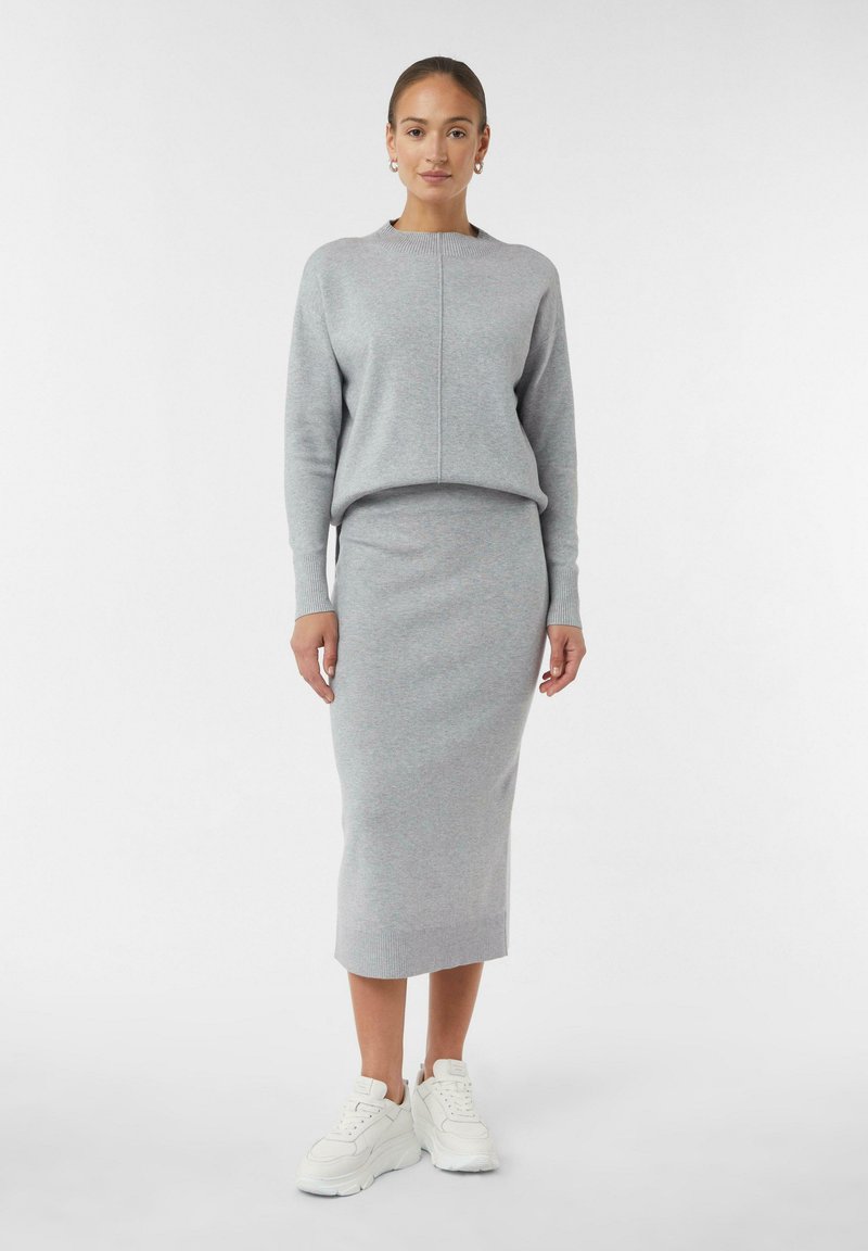 Maglione grigio lavorato a maglia con scollo rotondo e polsini a coste, abbinato a una gonna finta lunghezza al ginocchio. Sneakers bianche completano il look.