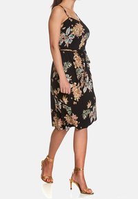 Černé květinové šaty s nastavitelnými ramínky, stahovací pasem a sukní ke kolenům. Vyznačují se živými květinami v oranžové, modré a zelené barvě.