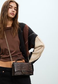 Borsa a tracolla marrone con motivo, dotata di manico e catena. Presenta una chiusura a patta e un design impresso su materiale testurizzato.