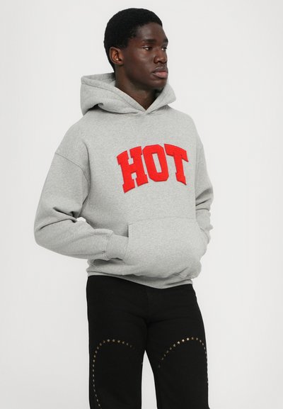 Haut à capuche gris avec un graphique rouge "HOT". Il présente une poche avant et une capuche avec cordon, associé à un pantalon noir orné de motifs d'étoiles dorées.