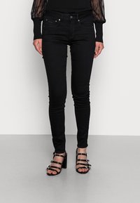 Jeans ajustados negros con una textura suave, que cuentan con cinco bolsillos y pasadores para cinturón. Combinados con sandalias de tacón alto negras con tiras.