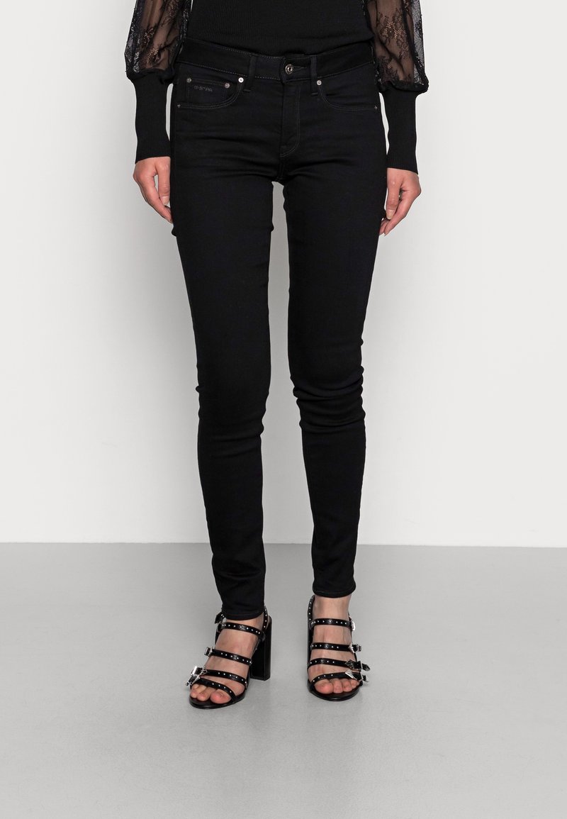Jeans ajustados negros con una textura suave, que cuentan con cinco bolsillos y pasadores para cinturón. Combinados con sandalias de tacón alto negras con tiras.