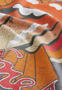 Színes anyag hullámos fekete-fehér mintákkal narancssárga és bézs háttéren, texturált, enyhén kopott megjelenéssel.