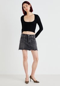 Haut noir à manches longues froncé associé à une mini-jupe en denim gris avec un ourlet effiloché et des coutures contrastées. Des talons en imprimé léopard complètent le look.