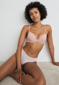 Lys rosa bh med underwire, glatte kopper og justerbare stropper, sammen med matchende høymidjestruser som har et mykt, minimalistisk design.