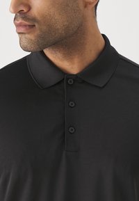 Svart polo tröja med mjuk textur, klassisk krage och tre knappar vid knappslån, som visar upp en strömlinjeformad design.