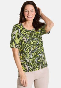 Blouse à manches courtes avec un motif tourbillonnant en vert, beige et noir. Fabriquée en tissu lisse, avec un col rond et une coupe décontractée.