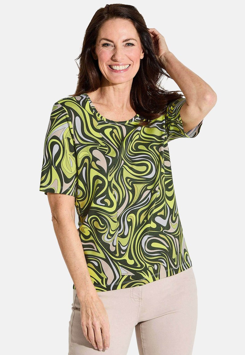 Blouse à manches courtes avec un motif tourbillonnant en vert, beige et noir. Fabriquée en tissu lisse, avec un col rond et une coupe décontractée.