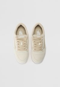 Beige Vans sneakers with a suede and canvas upper, round toe, flat laces, perforated detailing, and a white rubber sole.