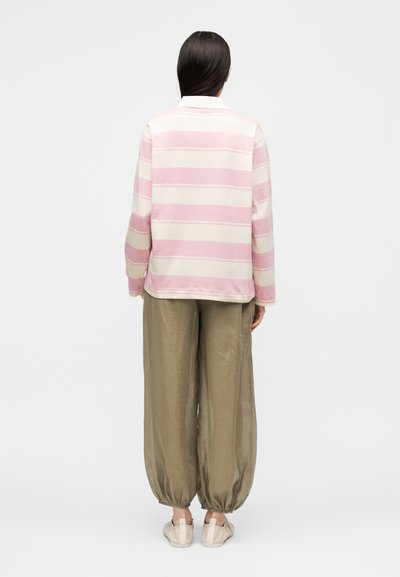 Άτομο που στέκεται ανάποδα, φορώντας ένα ροζ και λευκό ριγωτό μακρυμάνικο μπλουζάκι, φαρδιά χακί παντελόνια και ανοιχτόχρωμα παπούτσια.