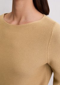 Beżowy sweter z okrągłym dekoltem, z teksturowanym wzorem i gładkim wykończeniem, podkreślający czyste linie i dopasowaną sylwetkę.