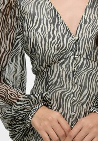 Blusa trasparente con motivo a strisce zebrato in nero e crema, con scollo a V profondo, maniche a sbuffo e dettagli con bottoni sul davanti.